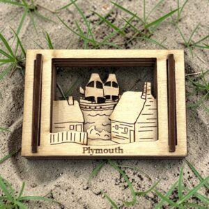 Plymouth, MA Matchbox Miniature resting in sand and beach grass, showing the layered wood ship and houses